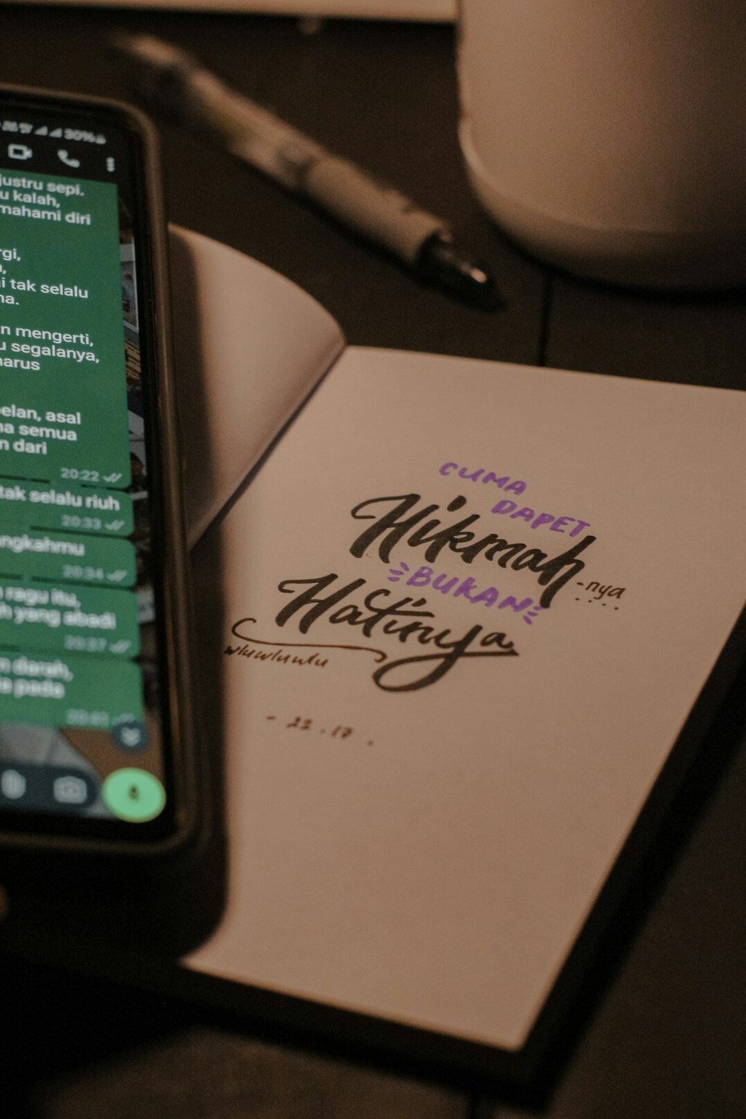 Hand writing notes in a notebook next to a phone on a desk