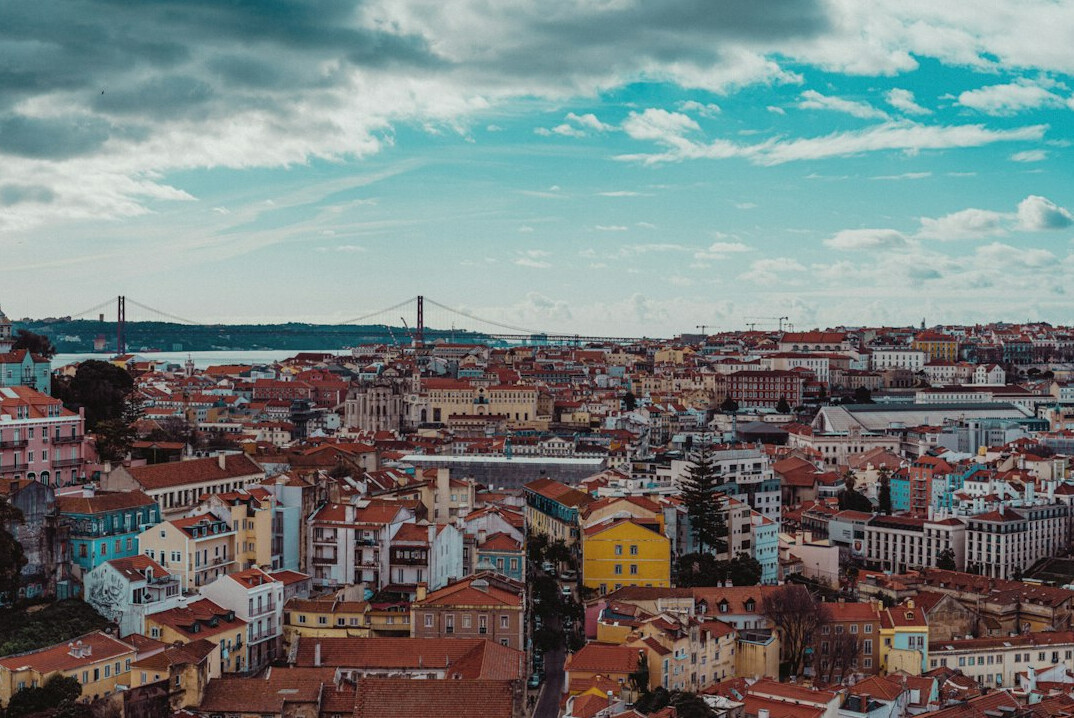 Investigative journalist's desk covered in documents with Lisbon skyline in the background